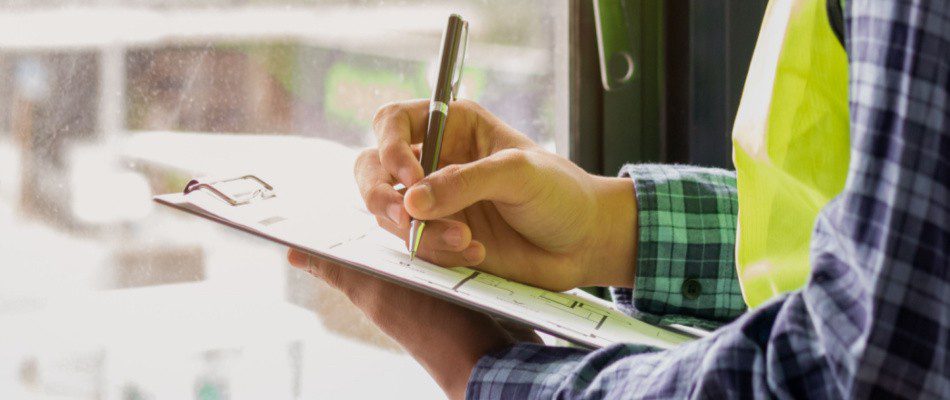 A man is writing on a clipboard in front of a window.