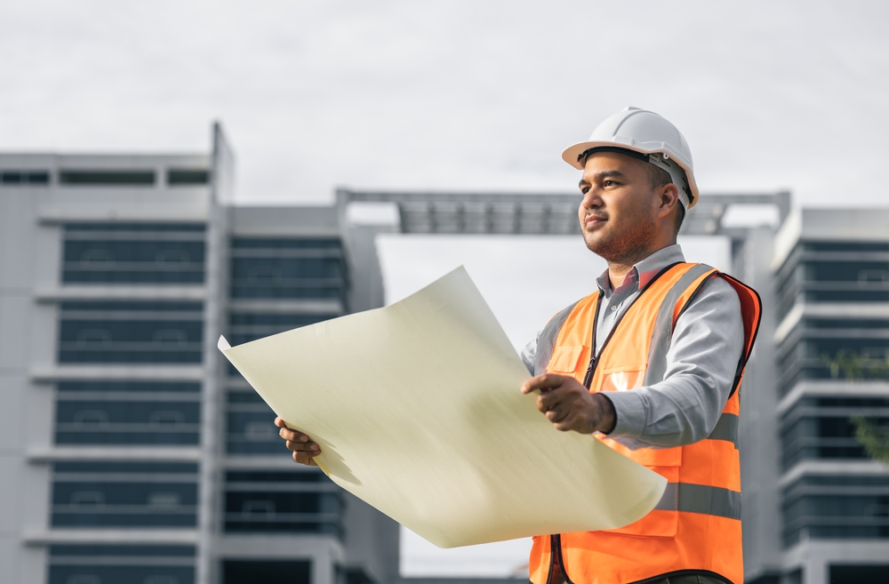 A construction worker holding a blueprint in front of a building.