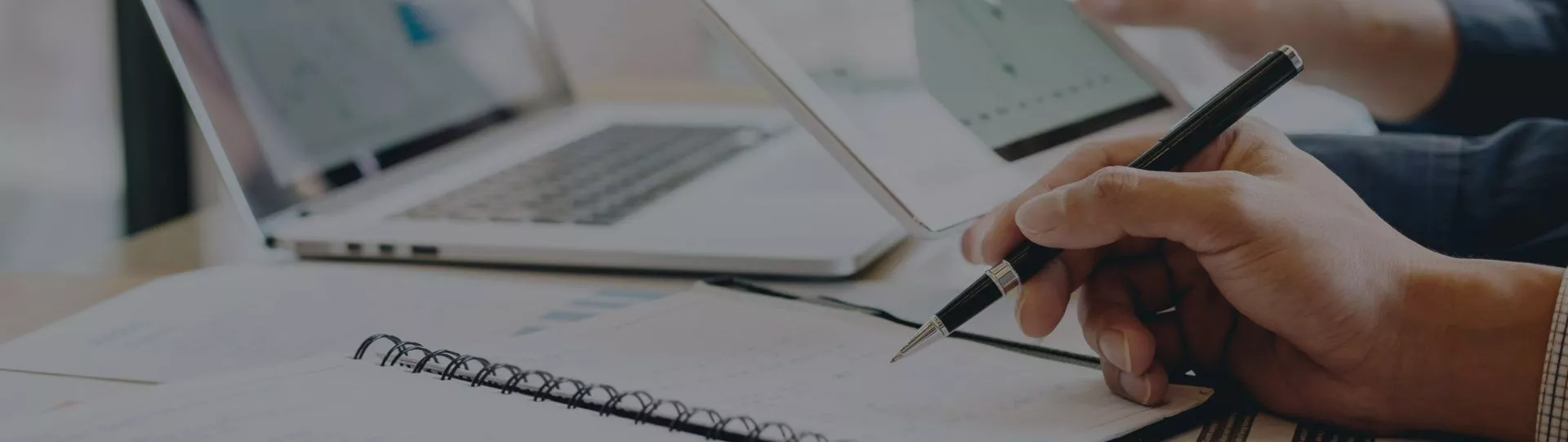 A person is writing on a notebook while sitting at a desk with a laptop.